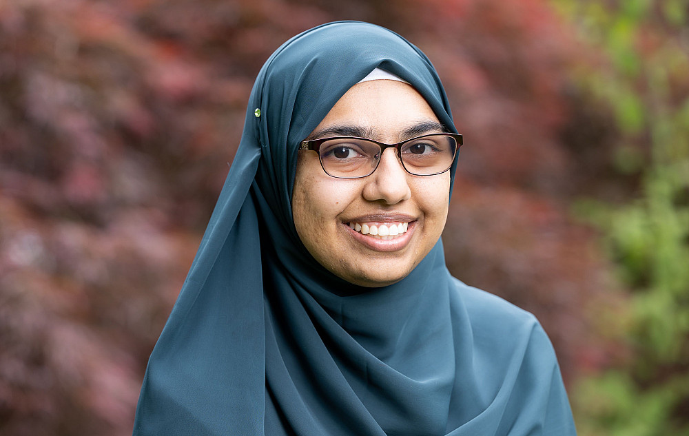 Nuzhat smiling at the camera, wearing glasses and a blue hijab.