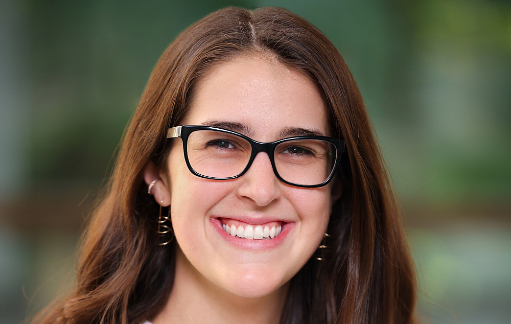 Raiven smiling at the camera. She is wearing a white top and black glasses.