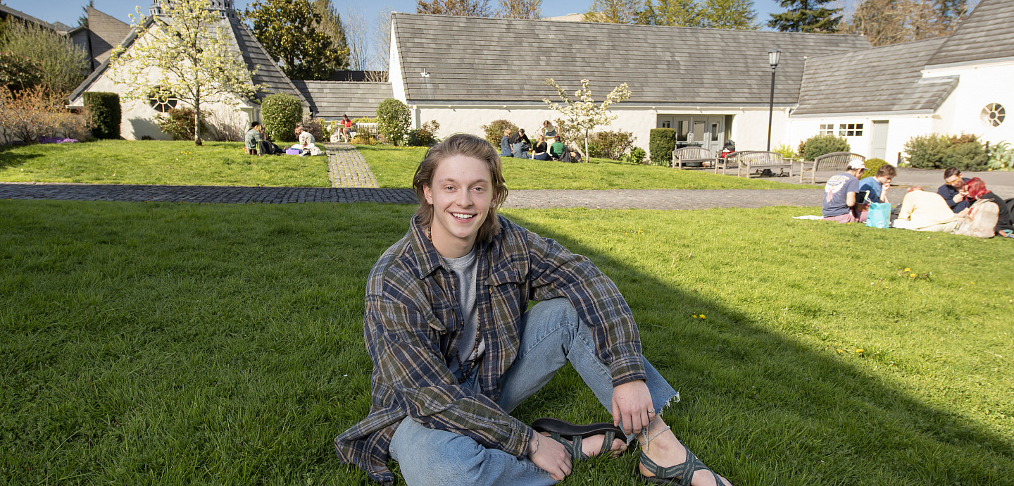 Bode sitting outside Albany Quadrangle. He is wearing a checkered shirt and blue jeans.