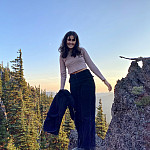 Lilah posing outside, surrounded by trees and a blue sky. She is wearing a light pink long-sleeve top and dark blue jeans.