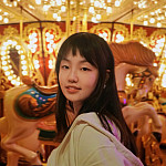 Polly smiling in front of a carousel. She is wearing a white top.