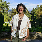 Meilin posing outside with Mount Hood in the background. They are wearing glasses and a white button-up shirt open over a black top.