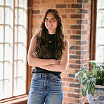 Morgaine posing inside near a window. She is wearing a black tank top and blue jeans.