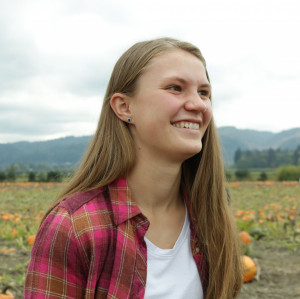 Katya smiling outside wearing a red flannel shirt over a white top.