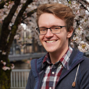 Karl smiling outside, wearing glasses, a plaid button-down shirt, and a blue jacket.