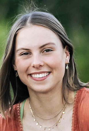 Torrey smiling at the camera outside. She is wearing an orange top.