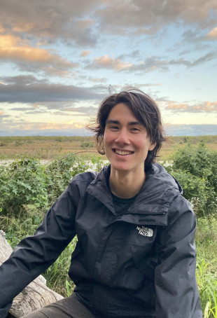 Ryan smiling outside at sundown, wearing a black rain jacket.