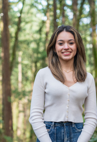 Kiara smiling at the camera outside, wearing a white top and jeans.