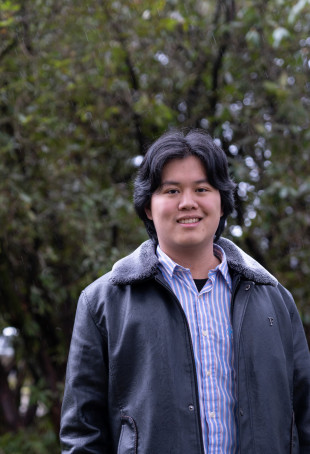 Tanner posing outside wearing a leather jacket and button-up shirt.