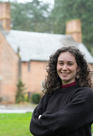 Lena posing in front of the Manor House, wearing a dark grey sweater.