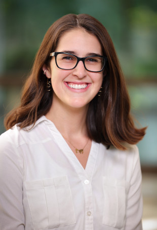Raiven smiling at the camera. She is wearing a white top and black glasses.