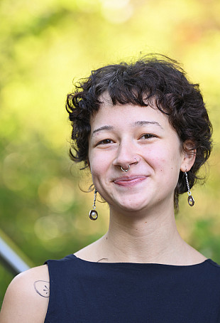 Audrey smiling at the camera against an outdoor green background, wearing a tank top.