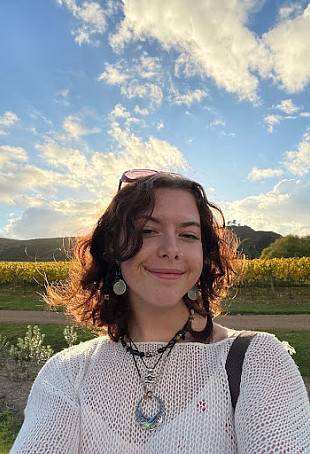 Ella smiling in front of a green field on a sunny day.