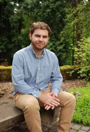 John smiling outside, wearing a blue button-down shirt and khakis.