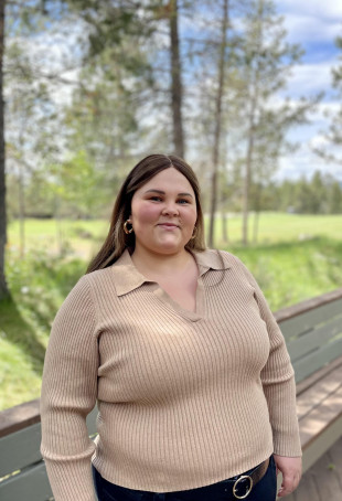 Emily posing outside, wearing a tan shirt and dark pants.