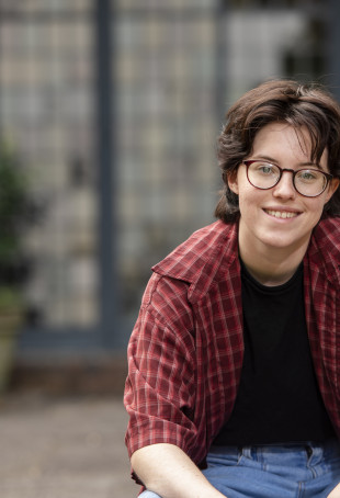 Apollo smiling outside, wearing a red plaid shirt over a black t-shirt.