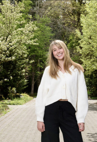 Grace posing outside in a white top and black pants.