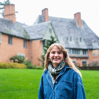 Beau posing in front of the Manor House, wearing a blue jacket and scarf.