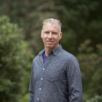 Elliott posing outside, wearing a blue button-up dress shirt.