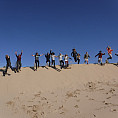 Participants jump in the air with hands up on the sand dunes.