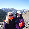 Image shows two students smiling, standing in front of a view of the Wallowa Mountains
