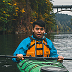 Picture shows a man wearing a blue jacket and yellow life-jacket sitting in a green kayak