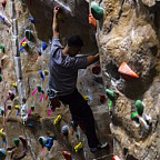 A student climbs on an indoor rock wall with ropes and harness