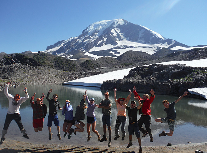 Image shows: a group of people jumping in the air with a view of Mt Adams behind them.