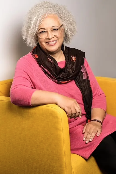 An image of Valerie White smiling as she sits on a yellow chair