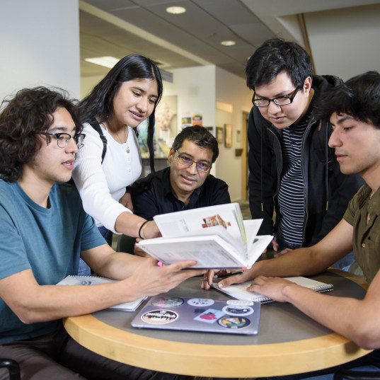 Professor Freddy Vilches at a round table with 4 other students looking over study materials.