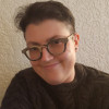 A photo of a woman with short hair wearing thick-rimmed glasses and a dark sweater