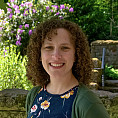 Stephanie is a Caucasian female presenting person with long curly brown hair. She is wearing a green cardigan sweater with a teal shirt w...