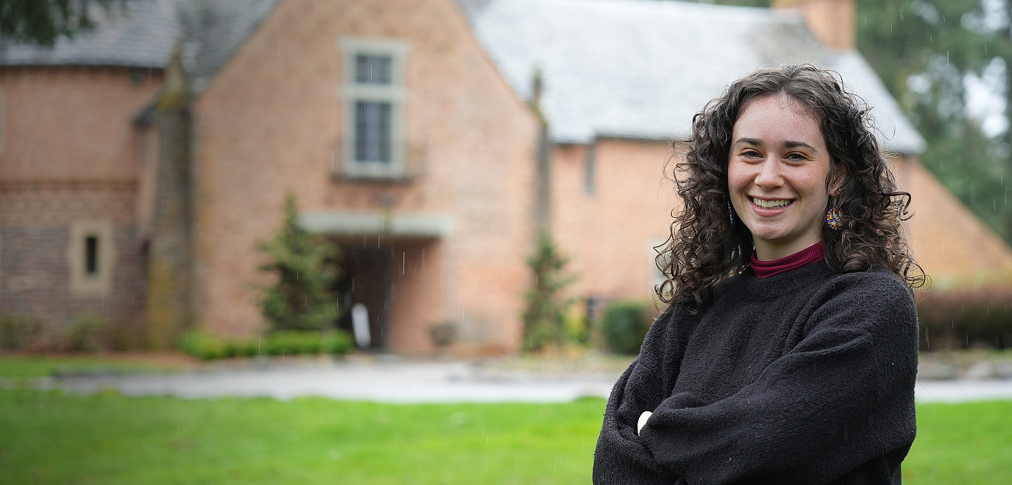 Lena posing in front of the Manor House, wearing a dark grey sweater.