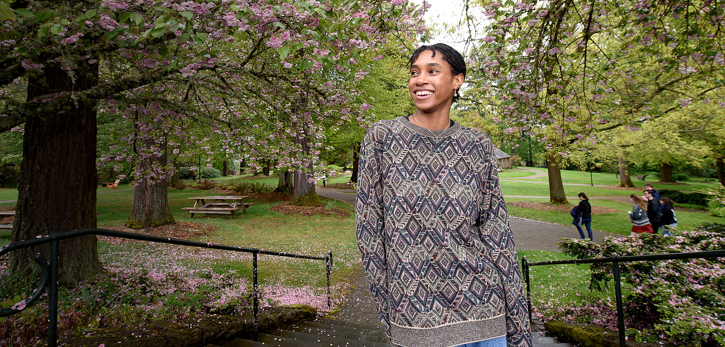 Jermisha smiling outside by cherry blossom trees, wearing a gray sweater.