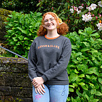Piper posing outside near stone steps with lots of greenery and white flowers behind her.
