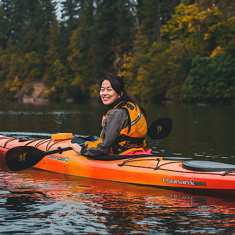 A student smiles at the camera while in a kayak on water.