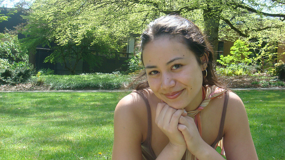 Jodi smiling at the camera with her hands under her chin. She is outside on a green lawn.