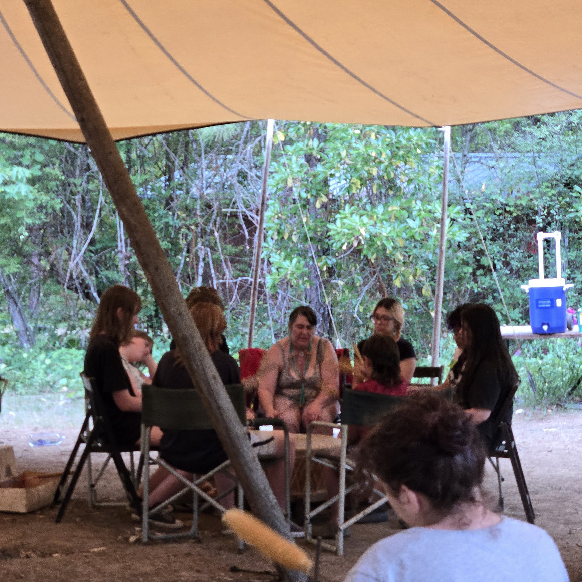 Campers sitting in a drum circle under a tent.