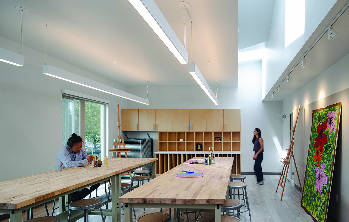An art room. A person sits at a high desk drawing on paper.