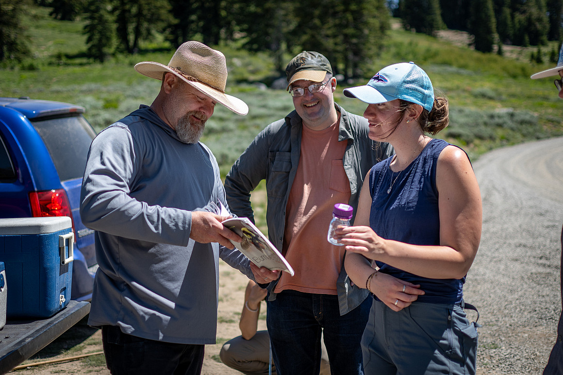 Three people stand together outside, looking at a research book.