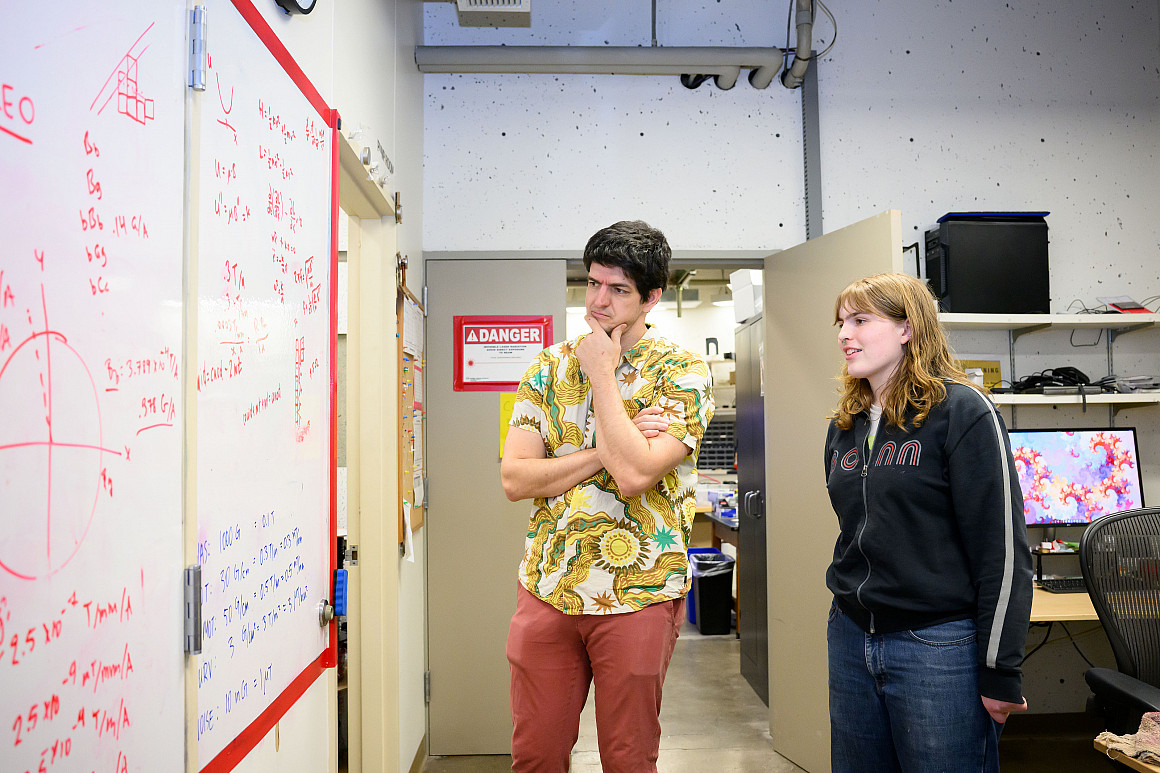 A professor and student stand at a white board.