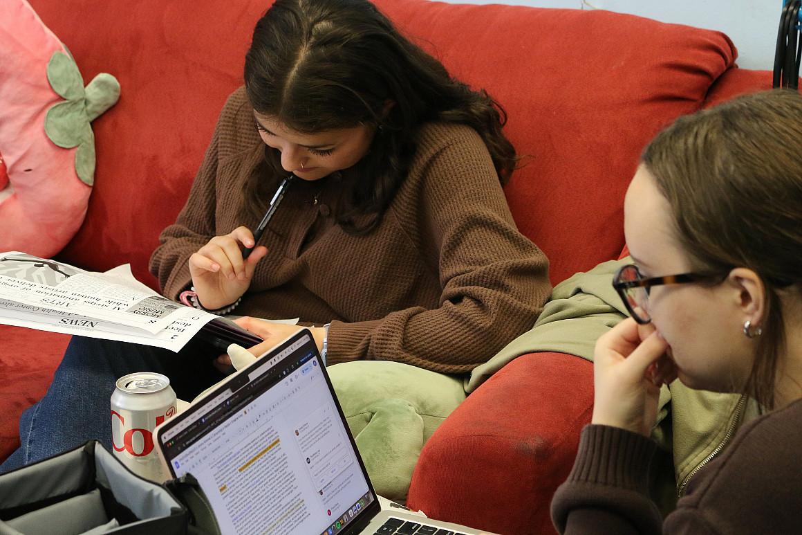 Two students working on laptops while sitting on couches.