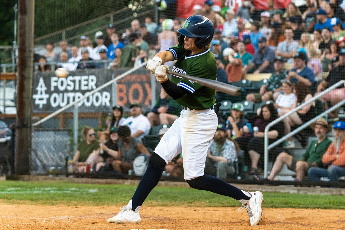 A baseball player hits a ball with a wooden bat.