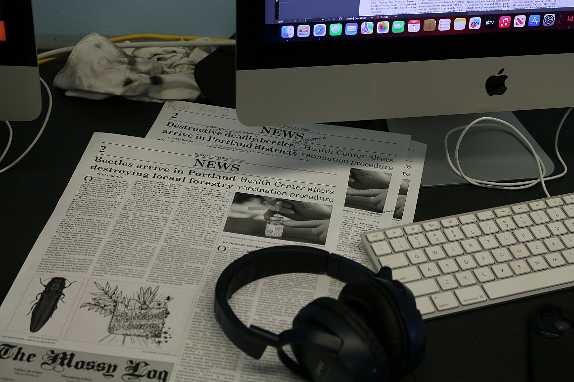 Photo of newspapers stacked up with headphones on top, near a computer.