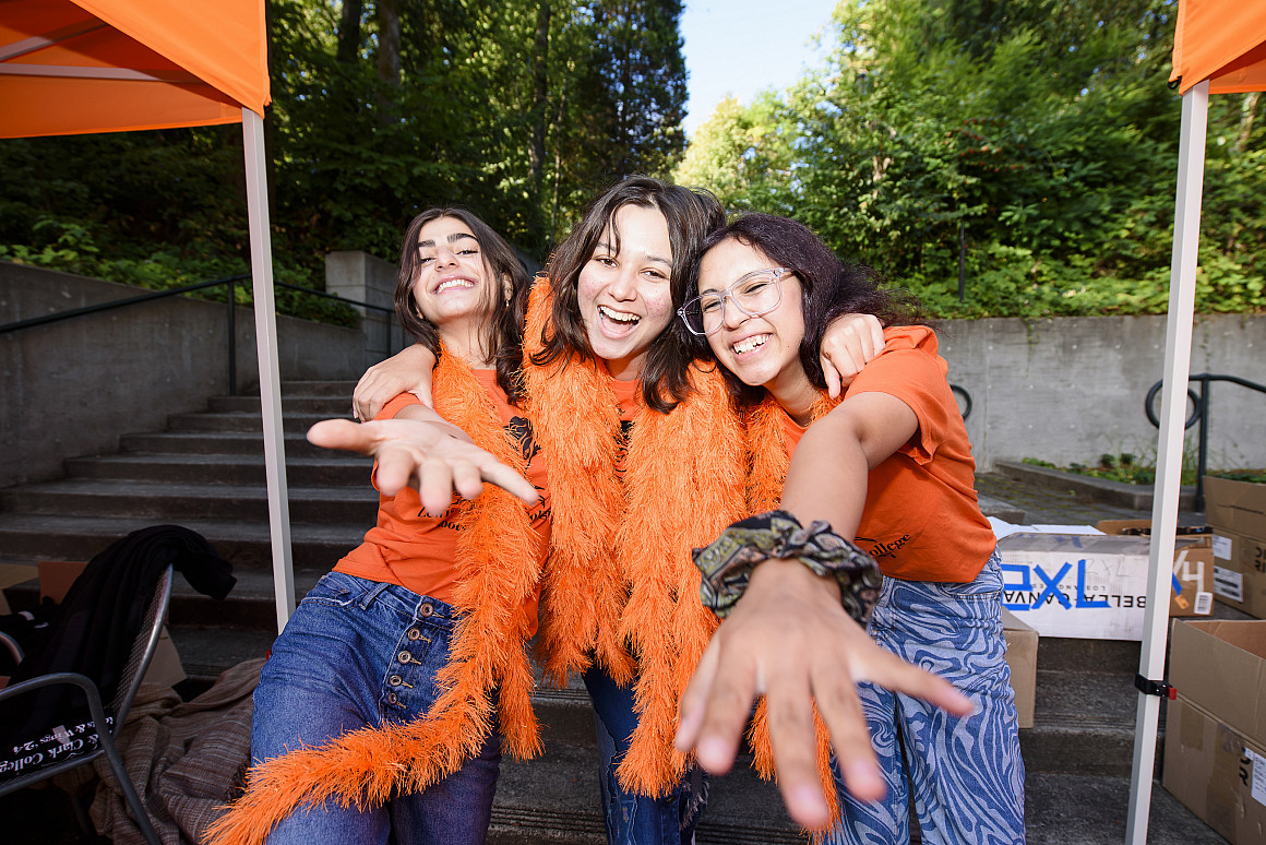 Three students smiling and reaching their hands out toward the camera.