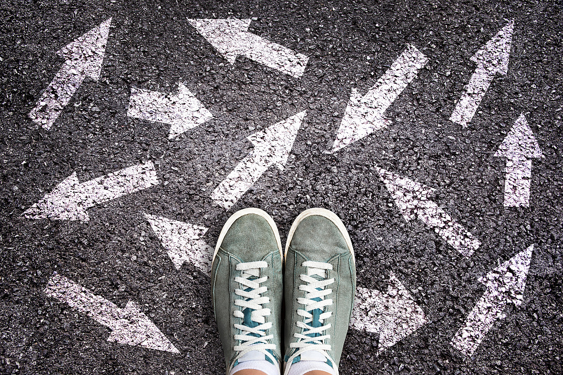 Sneaker shoes and arrows pointing in different directions on asphalt ground, choice concept