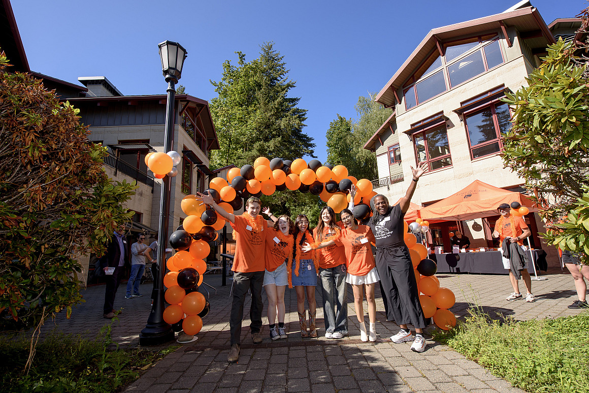 Students and President Holmes-Sullivan posing with their arms outstretched under a balloon arch.