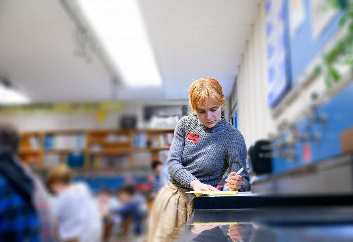 A student leaning on a table, writing in a notebook.
