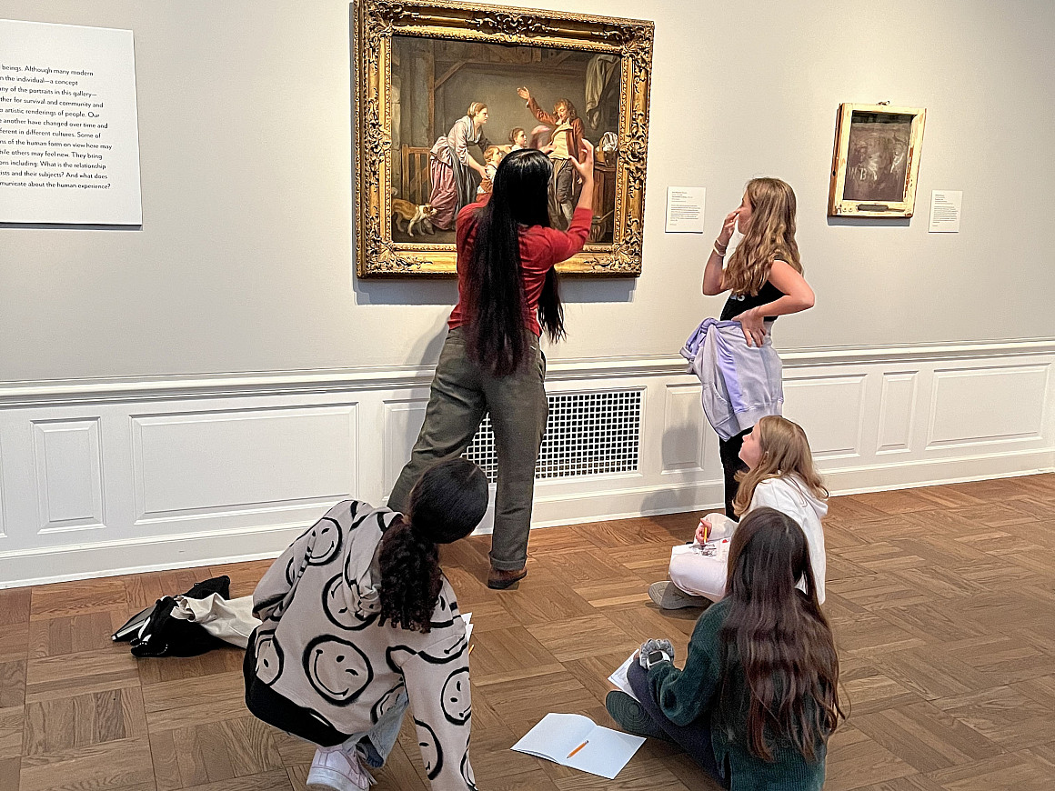 A group of students in front of a painting. One is reaching up and touching it.