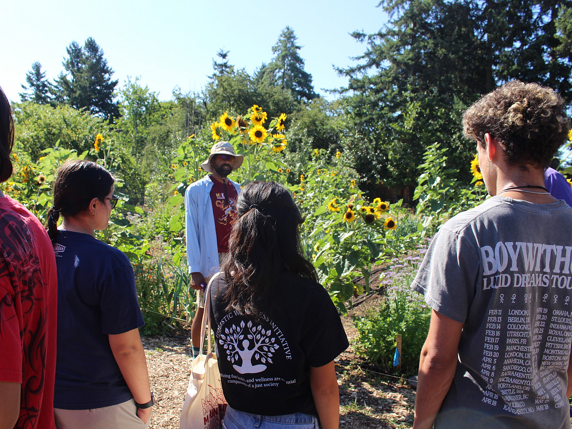 Students standing outside on a farm, listening to a man talk.